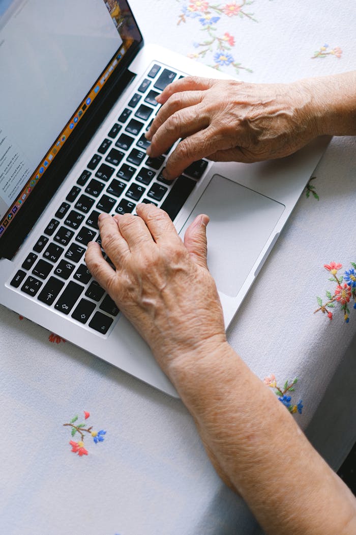services-01 Elderly hands typing on a laptop keyboard at home, promoting digital literacy among senior adults.