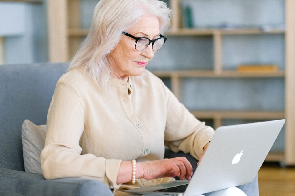 pexels-photo-5257246 Senior woman sitting indoors using a laptop for online activities.