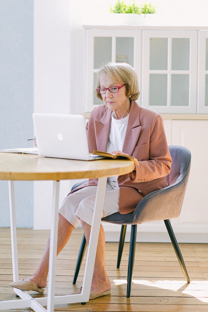 about-01 Elderly woman focusing on work using a laptop in a bright indoor setting.