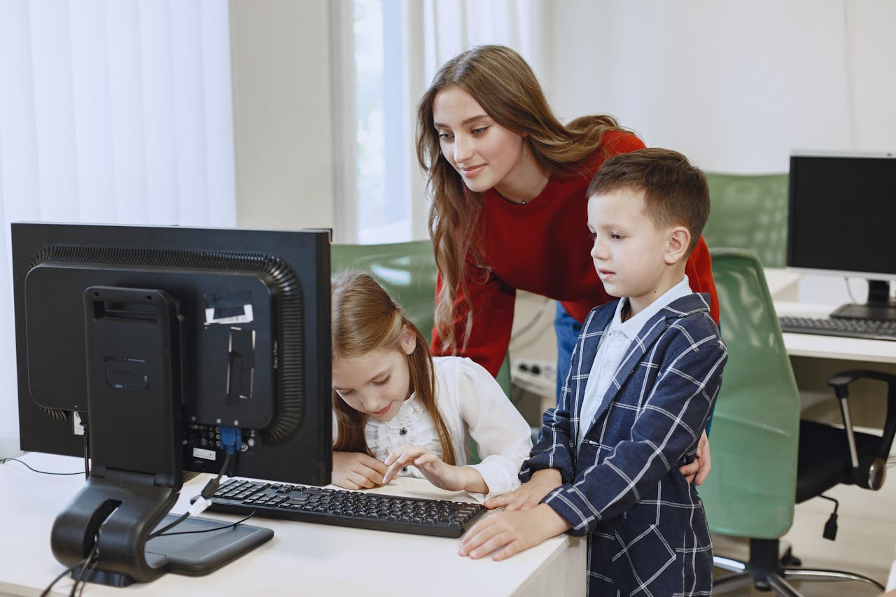services-03 A teacher guides two children using a computer in a classroom setting.