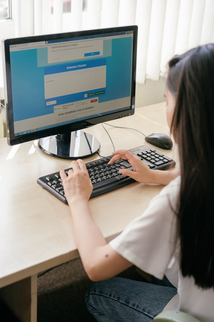 gallery-1 A student typing on a computer in a bright classroom for e-learning or research.